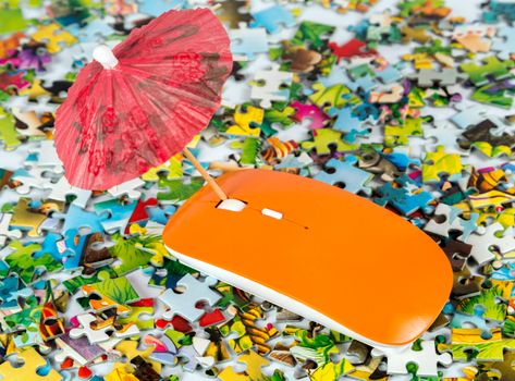 orange computer mouse with umbrella on the puzzle colored pieces background - concept trips tourist