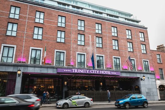 Dublin, Ireland - February 11, 2019: People and cars driving past the facade of the luxurious Trinity City Hotel in the city center on a winter day