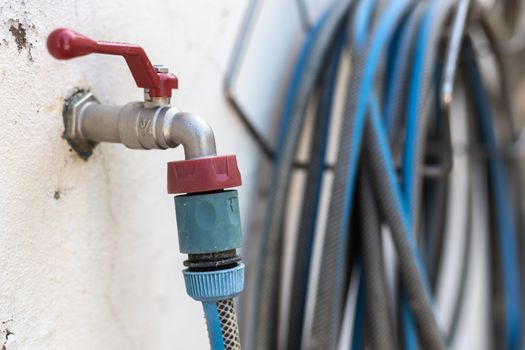 garden hose connected to a tap on a white wall with worn paint