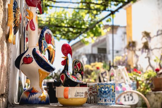 Obidos, Portugal - April 12, 2019: City rooster, cups, bowls and various souvenir items on the display of a souvenir shop in the historic city center on a spring day