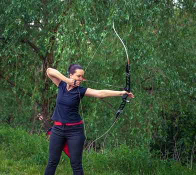 archery in nature. A young attractive woman is training in a bow shot with an arrow at a target in the woods.