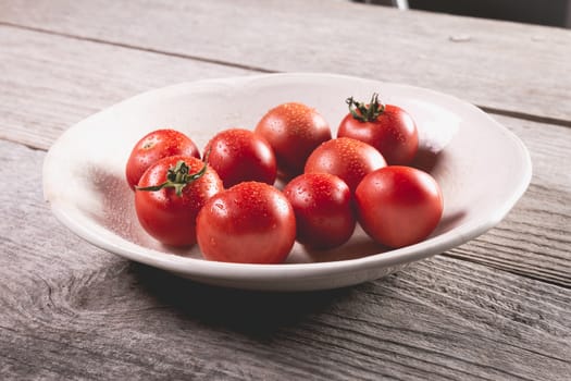 Plate of ripe tomatoes on wooden board background in studio