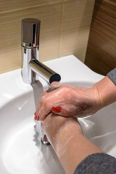 A woman is soaping her hands with soap under running water