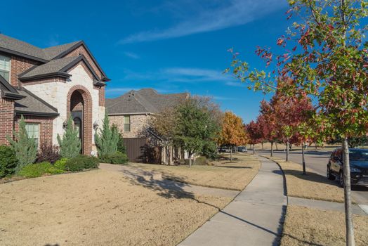 Front porch entrance of new development houses with parked car on residential street suburbs Dallas, Texas, America. Colorful fall foliage under sunny blue cloud sky.
