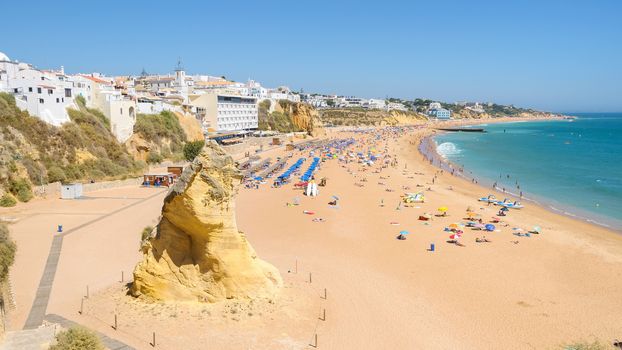 View of sunny public beach with sandstone rock in Albufeira, Algarve, Portugal