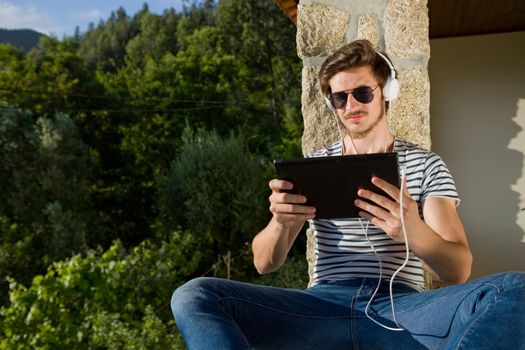 young man relaxing with a tablet pc listening music with headphones, outdoor