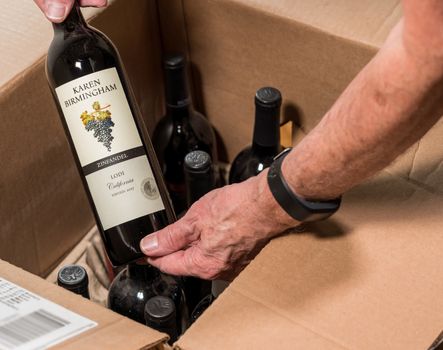 Morgantown, WV - 19 May 2020: Senior man looking at wine bottle from Karen Birmingham out of box delivered from Naked Wines