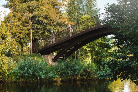 Beautiful and young girl stands on the wooden bridge in the green park. She looks at the beautiful nature.