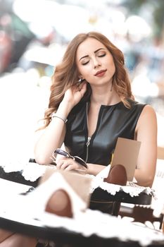 Attractive young caucasian woman sitting in street cafe, waiting for someone, having coffee, having great time. She wearing black stylish dress,