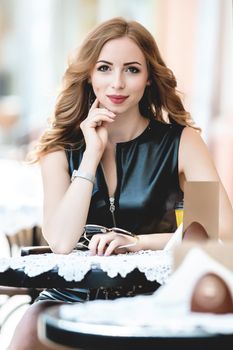 Attractive young caucasian woman sitting in street cafe, waiting for someone, having coffee, having great time. She wearing black stylish dress,