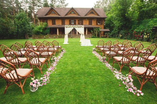 Outdoor wedding ceremony decoration setup. Path with petals, chairs decorated with colorful ribbons, white arch. wedding concept