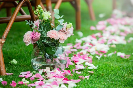 Outdoor wedding ceremony decoration setup. Path with petals, chairs decorated with colorful ribbons