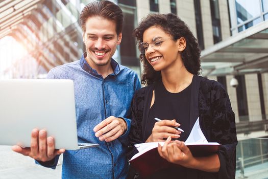 Two smiling colleagues are chatting in the street during lunch break near the building in the background.