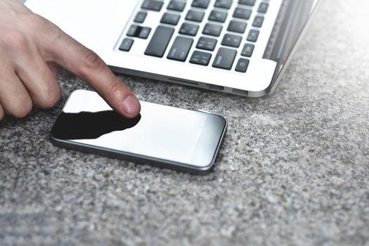 Cropped image of young woman downloading applications and multimedia programs by mobile smartphone, with laptop computer at street in modern city.