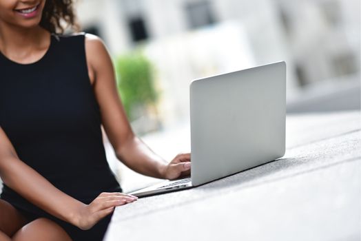 Young attractive mixed race girl with beautiful afro hair who is smiling looking at her laptop screen during video call. Young woman using laptop.
