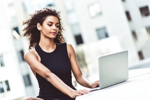 Young attractive mixed race girl with beautiful afro hair who is smiling looking at her laptop screen during video call. Young woman using laptop.