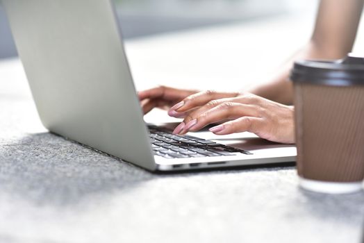 Young businesswoman sitting at street working with laptop, close-up photo. Business, education, lifestyle concept.