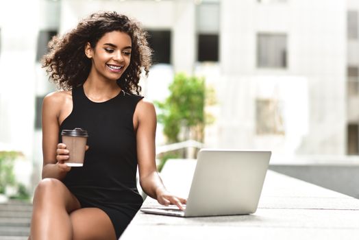 Young attractive mixed race girl with beautiful afro hair who is smiling looking at her laptop screen during video call. Young woman using laptop.