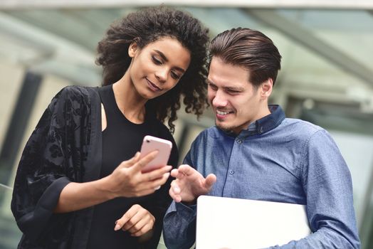 Business man and woman looking at smartphone together on building background in city outdoor feeling happy.