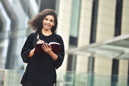 Charming Afro American beautiful happy female, making notes in notepad while walking outdoors on a city street. Education and business concept with space for text.