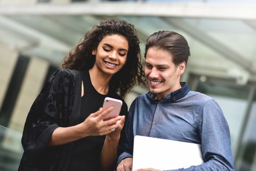 Business man and woman looking at smartphone together on building background in city outdoor feeling happy.