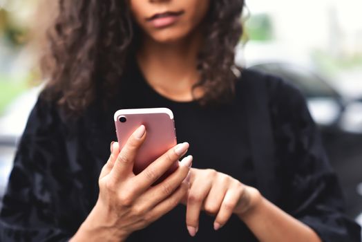 Close up portrait of beautiful young african american woman reading text message on mobile phone at street.