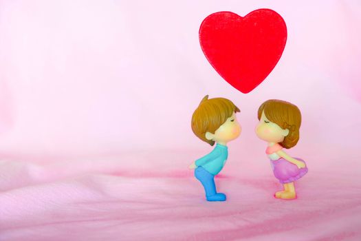 Miniature dolls of couple boy and girl kiss and have big red heart on above with pink background for Valentine's Concept