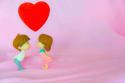 Miniature dolls of couple boy and girl kiss and have big red heart on above with pink background for Valentine's Concept