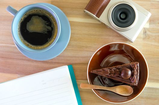 notebook, camera,  coffee, chocolate cake on wooden background