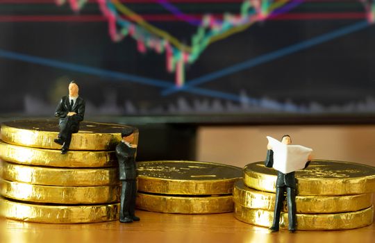 The miniature figure a group of business men sitting on top of pile stack of golden coins and some standing reading newspaper and discuss to other  with a Stock Market Techinical Graph Candlestick Background business success concept