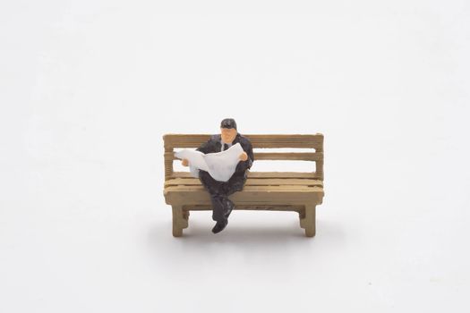 miniature businessman sitting reading newspaper in the bench isolate on white background