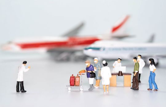 the miniature figure doll passenger in airport wearing mask to protect Coronavirus or Covid-19 walking to Disease Control point that have Doctor and nurse isolate on White background
