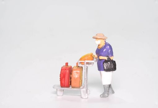 the miniature figure doll old lady passenger wearing face mask with travel suitcase and bag isolated on white background