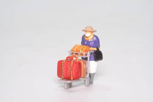 the miniature figure doll old lady passenger wearing face mask with travel suitcase and bag isolated on white background