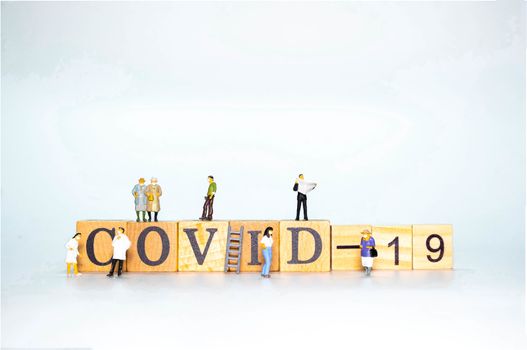 The Wooden Alphabet word COVID-19 with miniature figure doll of people and doctoe nurse wearing face mask  isolate on White background