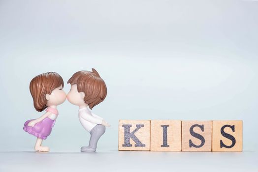 The Miniature doll of couple boy and girl kiss and have Wooden alphabet word KISS isolate on White background