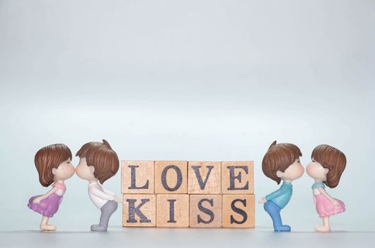 Miniature doll of couple boy and girl kiss and have Wooden alphabet word LOVE KISS isolate on White background