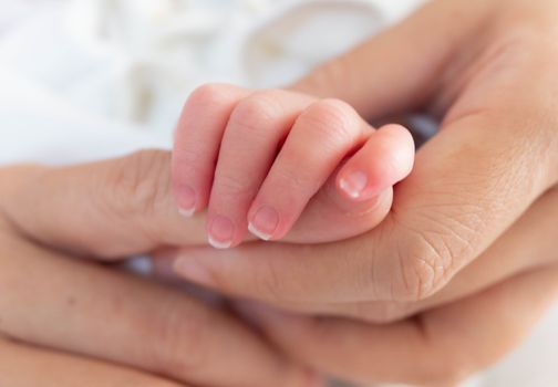 Hand of sleeping new born infant baby in the hand of mother close up on the bed