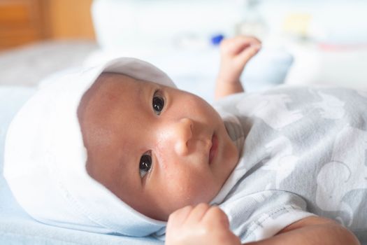 Portrait Photo of happy newborn baby infant with big black eyes lay down on the bed