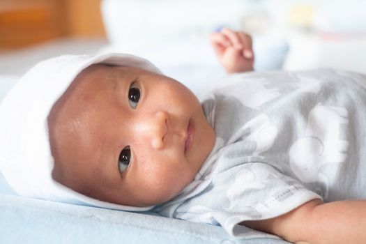 Portrait Photo of happy newborn baby infant with big black eyes lay down on the bed