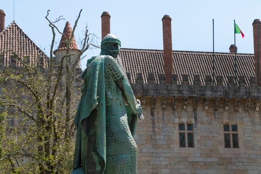 Guimaraes, Portugal - May 10, 2018: statue of the first king of Portugal, D. Afonso Henriques by the sculptor Antonio Soares dos Reis in front of the castle of Guimaraes that tourists are visiting on a spring day