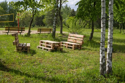 Rustic wooden table and benches made with pallets on the shore of a tranquil a lake surrounded by trees and greenery in summer sunshine