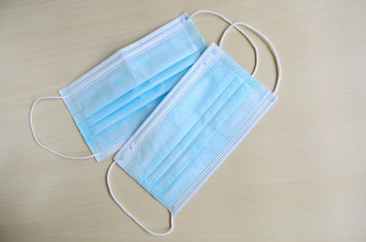 Surgical mask with rubber ear straps isolated on wooden background. Typical 3-ply surgical mask to cover the mouth and nose. Protection concept.