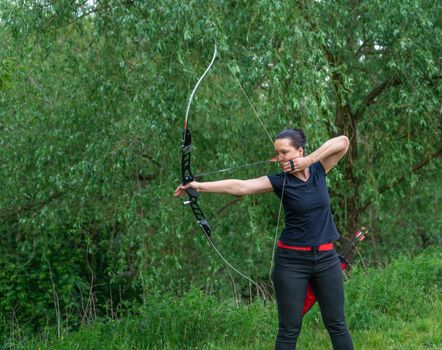 archery in nature. A young attractive woman is training in a bow shot with an arrow at a target in the woods.
