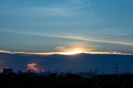 A sunset image with a cloud divides the line between the center of the image with the background as the building in the city.