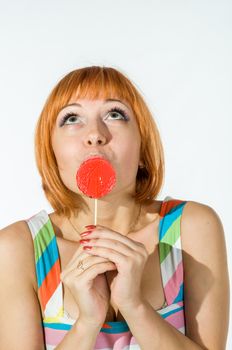 Colorful young woman with fantasy hair eating a red lollipop looking at camera. Beauty and makeup concept portrait isolated on white.