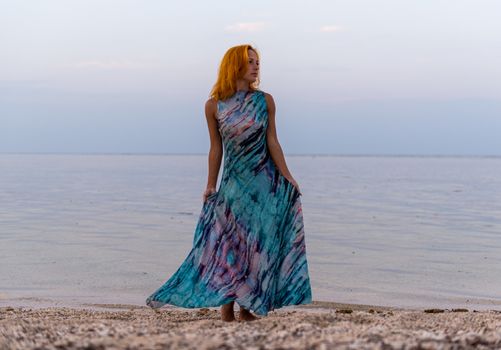 Young red woman wearing long dress on a beach