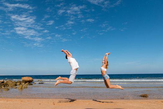 Happy caucasian couple having fun at the beach jumping