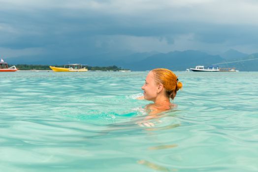 Woman at tropical island beach swimming in lush blue water