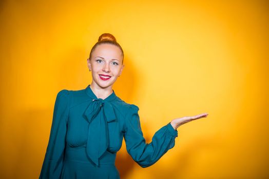 Happy cheerful redheaded girl presenting copyspace on her palm wearing green dress over yellow background